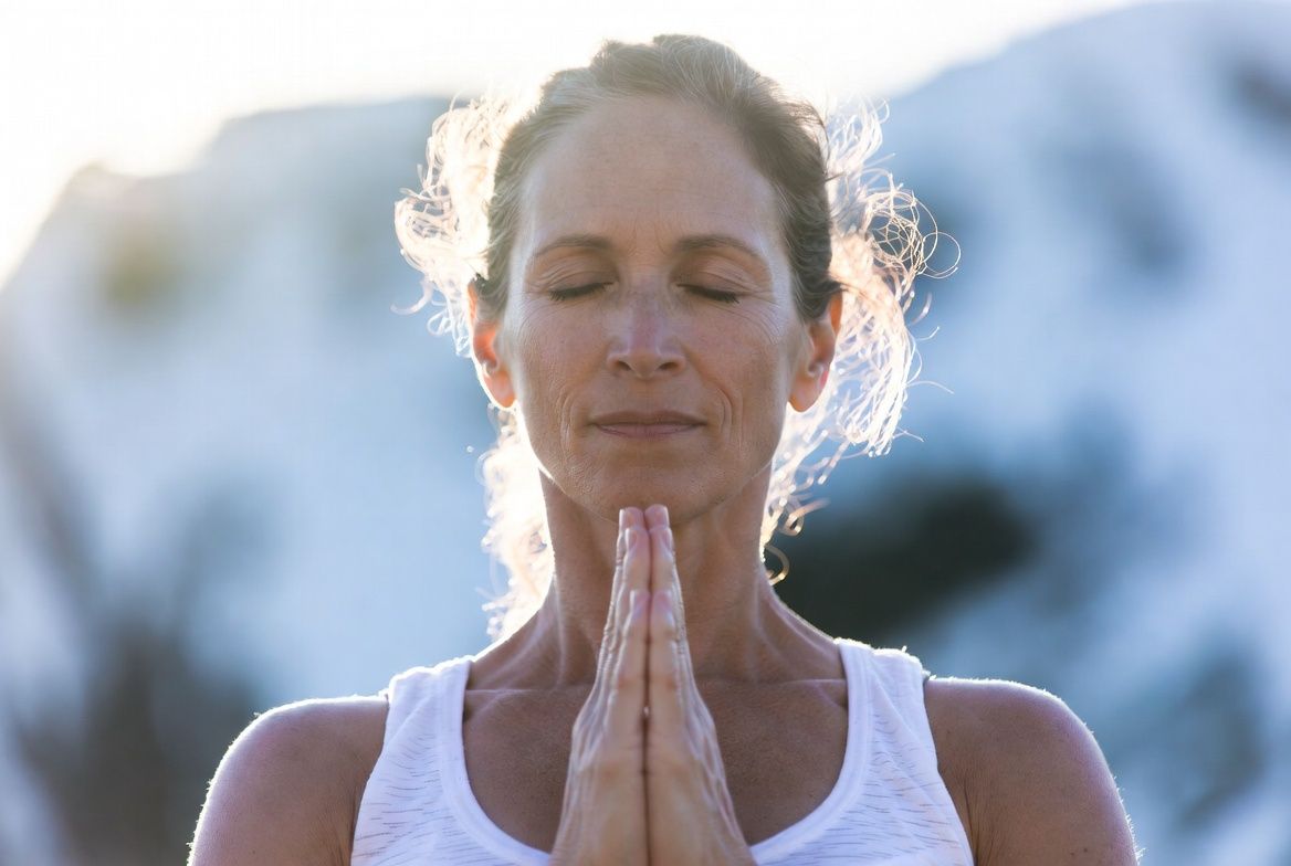Spiritual awakening meditation practice — woman meditating with eyes closed, hands in prayer position, soft morning light, wellness editorial